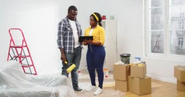 Genç Afro-Amerikan mutlu aile eşi ve kocası tamir işleri sırasında yeni bir dairede duruyorlar. Tablet üzerinde yazı yazıyorlar. Dekor seçiyorlar, ev dekorasyonu, dekorasyon odası, onarım konsepti.