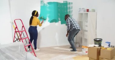 Afro-Amerikalı genç mutlu evli çiftin apartman dairesinde birlikte tadilat yapması. Karı koca boya fırçasıyla duvarları yeşile boyuyor. Ev yenileme, iyileştirme konsepti