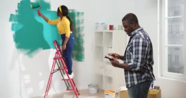 Yakışıklı, Afro-Amerikalı bir adamın portresi. Tablet cihazıyla yazı yazıyor. Karısı da yeşil renge boyuyor. Daire geliştirme, onarım, yenileme konsepti