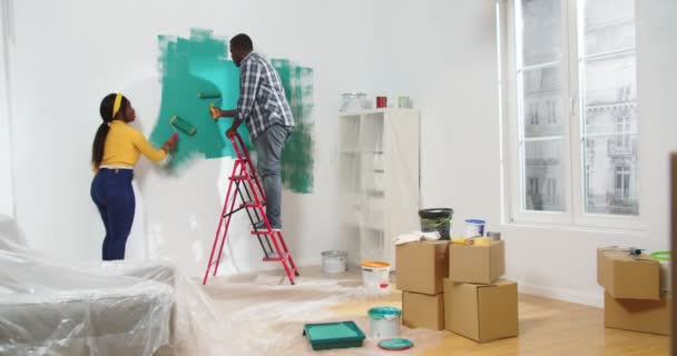 非洲裔美国人年轻夫妇的后背 他们的妻子和丈夫在新的房子里用彩绘滚笔画着绿色的墙 公寓翻新 装修概念 — 图库视频影像