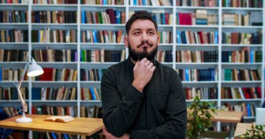 Kafkasyalı genç düşünceli bir adamın portresi kütüphane odasında duruyor ve bilgece bir bakışla düşünüyor. Erkek felsefe profesörü veya öğretmen bazı teorileri göz önünde bulundurun ve kameraya gülümseyin..