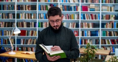 Gözlüklü, kütüphanede durmuş araştırma yaparken kitap okuyan beyaz bir genç. İncil 'de açık ilginç ders kitapları olan şık bir erkek öğrenci. Konsept çalış.