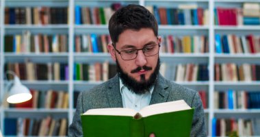 Gözlüklü, beyaz, yakışıklı bir adam kütüphanede ders kitabı okuyor. Erkek profesörü ya da araştırmacıyı elinde kitaplarla kitabevinde kitap okuyarak kapat. Konsept çalış