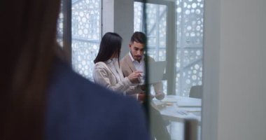 Genç erkek ve kadın ofis çalışanları dizüstü bilgisayarlarıyla odada duruyor ve ortak projeden bahsediyorlar. İş arkadaşları tavsiye istiyor. Kadın ve erkek çalışanlar tartışıyorlar..