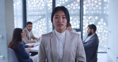 Genç, güzel bir Asyalı kadın, şirket çalışanı kameraya bir şeyler söylüyor iş yaparken video bloglamak gibi. Arka planda toplantı. Finansal video blogcusu konuşuyor ve açıklıyor. Kadın çevrimiçi koç.