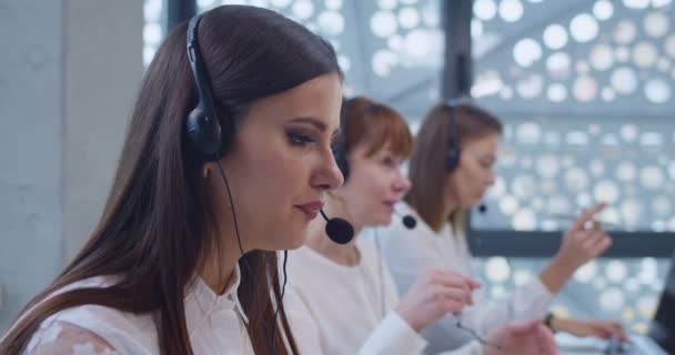 在呼叫中心与客户交谈时 紧盯着戴耳机的年轻白人女性 在线支助办公室的女操作员 帮助解决在线销售经理的技术问题 — 图库视频影像