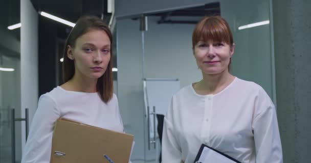 两个白人妇女同事的画像 年轻的和中年的白领同事站在坚实的走廊上 手里拿着文件夹 看着相机 在职的公司女工作人员 — 图库视频影像