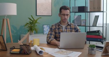 Gözlüklü genç beyaz adam ofisteki bilgisayarın başında çalışıyor ya da sıcak çay ya da kahve yudumlarken evde..