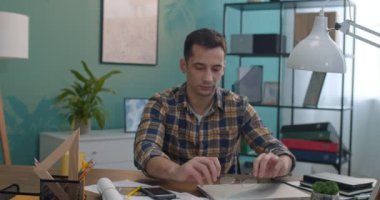 Beyaz, yakışıklı genç bir ofis çalışanı masada otururken gözlük takıyor ve kameraya bakıyor. Portre çekimi.