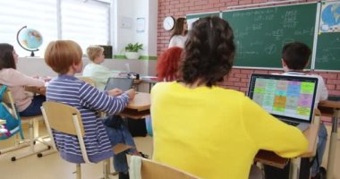 Kendine güvenen beyaz kadın öğretmen masadan kalkıp sınıftaki tahtaya geliyor. Resmi olarak çekici bir kadın geometri dersindeki öğrencilere yeni formülü açıklıyor..