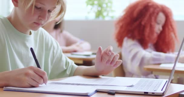 高加索聪明的少年学生坐在教室的书桌前 用复印机书写 用笔记本电脑学习 时间在学校 聪明的男孩在上课时学习 而且很集中 — 图库视频影像