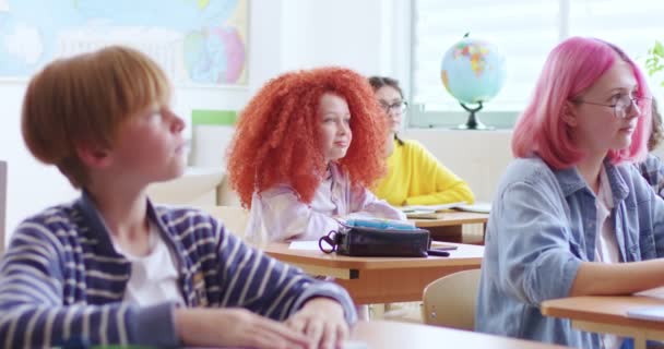 可爱的小聪明的女学生 一头红卷卷发 坐在教室里和其他青少年学生一起 举手回答课上的问题 聪明的小女孩学习学校的概念 — 图库视频影像