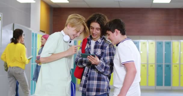在学校走廊休息的时候 三个男孩在数字智能手机上看电影 快乐的男同学穿着休闲装 课后自由自在 — 图库视频影像
