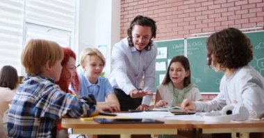 Yuvarlak masada oturup erkek öğretmenlerle el ele tutuşan mutlu ilkokul çocukları. Eğitim sisteminde modern yaklaşım.