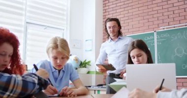 Kafkasyalı zeki çocuklar sınıflarında masa başında oturup egzersiz ve görevler yazıyorlar. Erkek öğretmen öğrencilere gelir ve onlara görevleri için tablet verir. İnteraktif eğitim. Sınıflar konsepti.