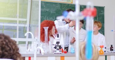 Koruyucu laboratuvar önlüğü ve gözlüklü kimya öğretmeni. Laboratuvarda ilkokul öğrencilerine ders veriyor. Göz bebekleri çeşitli sıvıları tüplerde karıştırma tepkisini inceliyor..