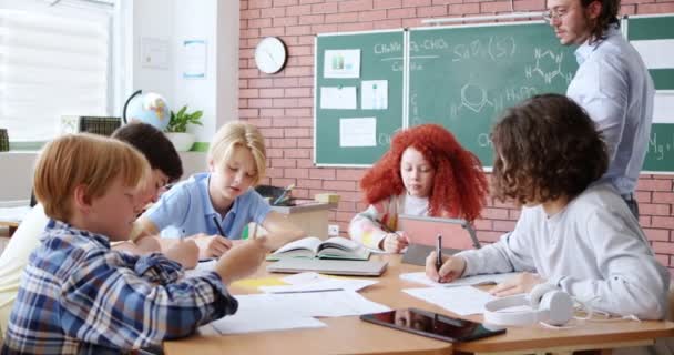 小学课堂上 快乐的男女学生记笔记和使用现代小玩意 白种人老师手里拿着数码平板电脑教孩子 — 图库视频影像