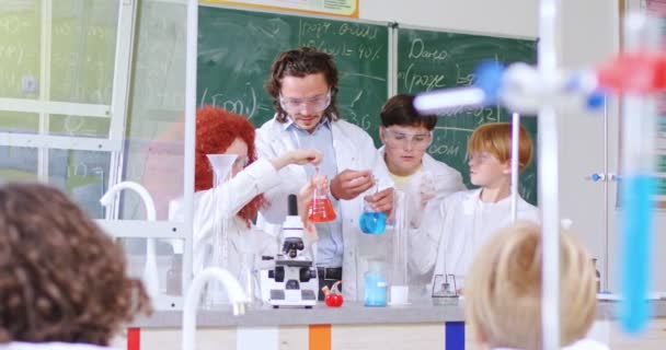 白人青少年在化学课上与年轻的男老师一起做化学实验 学生学校的实验室 管子和液体 — 图库视频影像