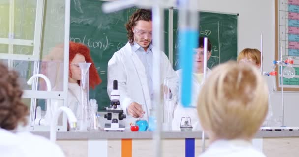 化学在学校的概念课 白种人男老师在课堂上给孩子们做化学实验 并给他们带蓝色液体的管子 儿童实验课 — 图库视频影像