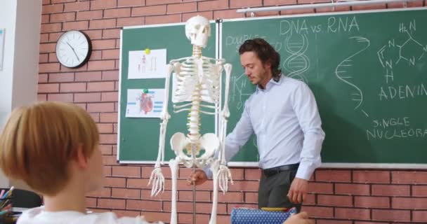 聪明的高加索老师通过展示骨架向好奇的小学生解释人体解剖学 科学和教育的概念 — 图库视频影像