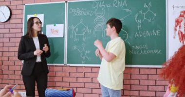 İlkokulun sevgili bayan öğretmeni dikkatle dinleyen okul çocuğu tahtanın yanındaki DNA yapısı hakkında cevap veriyor. Sınıftaki öğrenciler için biyoloji dersi.