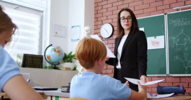 Beyaz kadın biyoloji öğretmeni öğrencilere sınav kağıtlarıyla bok dağıtıyor. Okuldaki sınavlar. İnceleme konsepti. Sınıftaki çocuklar için biyoloji ya da kimya testi. Eğitim.