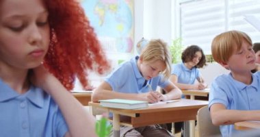 Mavi okul üniformalı erkek ve bayan öğrenciler masalarında oturan beyaz bayan öğretmenler kontrol işlerini başarıyla yapıyorlar. Modern okulda öğrenme süreci.