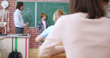 Kafkas ergen okul çocuğu, sınıfın önünde ekoloji hakkında konuşma yapıyor. Erkek öğretmen, çevreyi kurtarmakla ilgili haberi olan bir genci dinliyor. Okulda. Öğrenme konsepti. Öğrencilerin arkası..