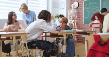 Kafkasyalı ergenler, akademisyenler ve liseli kızlar derslere ara verirken sıralarında oturup konuşuyorlar. Genç erkekler ve kızlar sınıfta dinlenirken sohbet edip oynuyorlar..