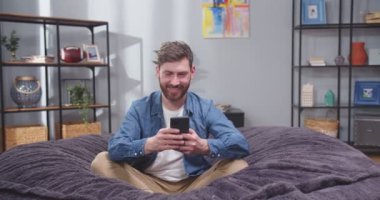Kanepede elinde akıllı telefonuyla yetişkin bir adamın portresini yakın plan çek. Erkek, sosyal medyayı zımbırtıda kaydırıyor. İşten sonra kanepede telefonla dinlenen bir adam. Yavaş çekim videosu. Kamera yuvarlak çekim 360.