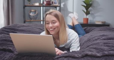Kanepede dizüstü bilgisayarla yatan yetişkin bir kadının portresini yakından çek. Kadın, sosyal medyada bir zımbırtıda kayıyor ve gülüyor. İşten sonra bilgisayar başında dinlenen bir kadın..