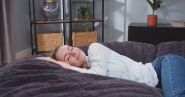 Kanepede sarılan yorgun, beyaz bir kadının yan görüntüsü. Yorgun bir kadın işten sonra dinleniyor. Rahatlama kavramı, tasasız. Yavaş çekim videosu.