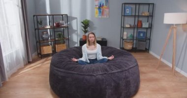 Kafkasyalı sarışın kadının kanepenin üzerinde nilüfer çiçeği pozu verirken uzaktan çekilen görüntüsü. Rahatlama ve meditasyon konsepti. Kişisel bakım, öz farkındalık konsepti. Kamera yakınlaştırılıyor. Yavaş çekim videosu.