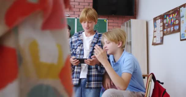 两名高加索少年学生在学校课间休息时玩智能手机和聊天 朋友们一边玩手机一边聊天 上学的生活 — 图库视频影像