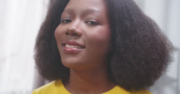 アフリカ系アメリカ人の女性の顔の横の肖像画を閉じます 女の子は歯で微笑み カメラを見つめている 黄色いセーターの女性 幸せな人たちのコンセプト スローモーションビデオ — ストック動画
