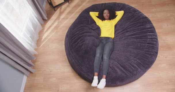 非洲裔美国女性躺在沙发上 双手交叉地把头靠在天花板上 俯瞰全景 累坏了的女性下班后休息 休息的概念 无忧无虑 慢动作视频 — 图库视频影像