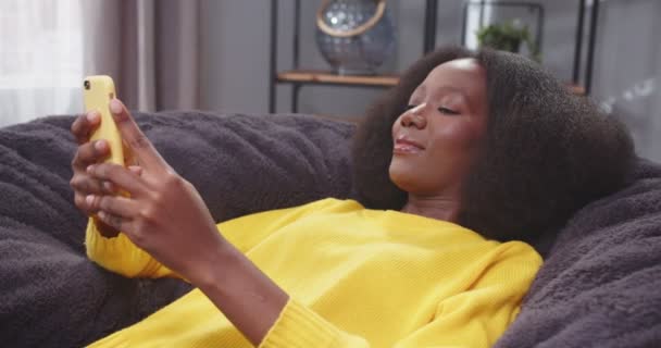 Κοντινό Πλαϊνό Πορτραίτο Αφροαμερικάνας Ξαπλωμένης Καναπέ Πληκτρολογώντας Και Κινητό Γυναίκα — Αρχείο Βίντεο