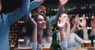 Cuma gecesi genç beyaz erkek ve kadınların barda ponpon kız hareketleri yaparak vakit geçirdiği yakın çekim. Amigo kızlar. Barda oynanan bir maçta taraftarlar takımı destekliyor.