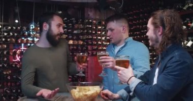 Bir grup genç adam barda takılıyor, bardakları tokuşturuyor ve bir kase abur cubur eşliğinde bira içiyor. Üç arkadaş güzel sohbet ediyor, gülümsüyor ve kafa sallıyor..