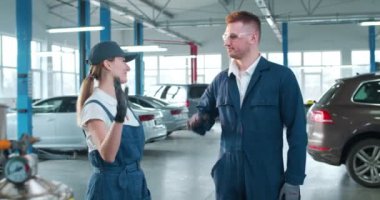 Kafkasyalı neşeli genç adam ve kadın, üniformalı oto tamircileri, gözlükler ve ingiliz anahtarı birbirlerine beşlik çakıyor ve kameraya gülümsüyorlar. Portre. Erkek ve kadın teknisyenler hizmetinizde..