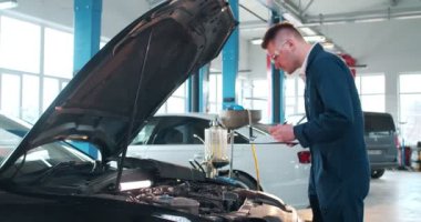 Üniformalı ve gözlüklü beyaz erkek tamirci otomobil servisinin onarımıyla ilgili belge dolduruyor. Aracın motorunu tamir eden ve fatura kesen genç adam. Çalışma konseptini korumak.