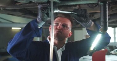 Beyaz, üniformalı erkek tamirci, araba tamircisiyle araba yıkama servisinde çalışıyor. Genç adam motoru tamir ediyor ve yeraltından İngiliz anahtarını çeviriyor. Konsepti korumak için. Tamir işi..