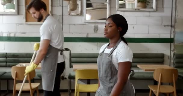 非洲裔美国年轻女服务员在餐馆大厅里与服务员擦拭餐桌 餐厅开业后开始营业 围裙上的漂亮女工 — 图库视频影像