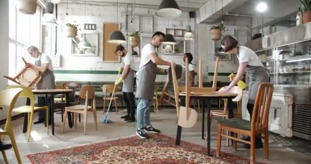 咖啡店里穿着灰色围裙的员工放下椅子 擦桌子和拖把地板 打扫房间 明亮舒适的咖啡店在上午开业前为顾客准备好咖啡 — 图库视频影像