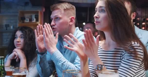 一群年轻的朋友在酒吧里聚会 看电视 支持运动队喝啤酒 男孩和女孩在失望中大喊大叫 蒙着脸 — 图库视频影像