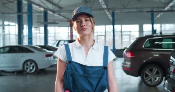 照片中 身穿制服 头戴帽子的白人美女站在大车库里 高兴地对着相机微笑 放弃了大拇指 漂亮的女机修工 — 图库视频影像