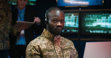 Ordudaki izleme odasında dizüstü bilgisayarın başında oturan ve sonra da kameraya bakan kulaklıklı Afro-Amerikan genç adamın portresi. Askeri merkezdeki erkek asker sevk memuruna yaklaş..