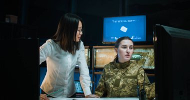 Asyalı genç bir kadın beyaz kadın askere bir şey gösteriyor ve onu ordu yönetimindeki deniz stratejisi konusunda eğitiyor. Kadınlar için Eğitim Deniz Askeri Merkezi.