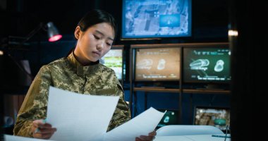Asyalı, üniformalı güzel bir kadın bilgisayar ekranının önünde oturuyor ve ordu gözlem odasında bazı belgeler yazıyor. Askeri merkezde çalışan bir kadın..