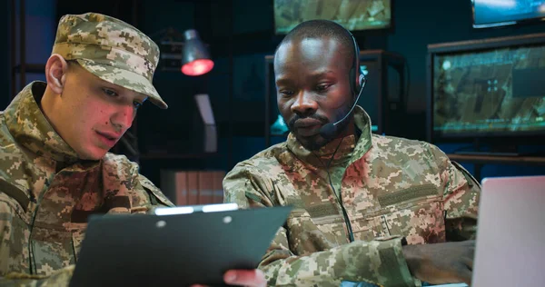 African American military dispatcher sitting in office and Caucasian male soldier bringing documents with new data and information. Two mixed-races army officers talking about secret operation.